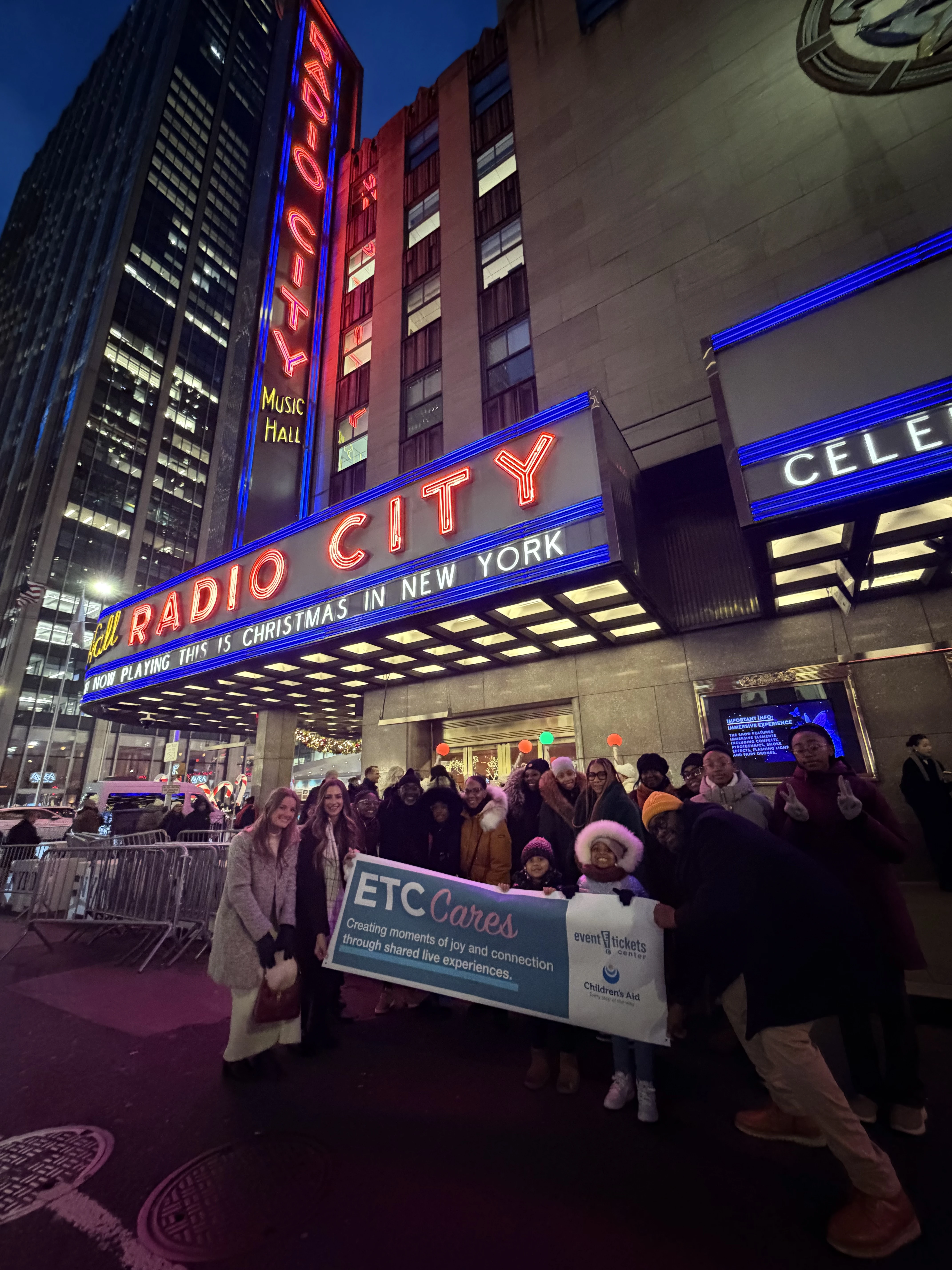 ETC team members grouped together in front of the entrrance to radio city music hall with the Children's Aid team and kids