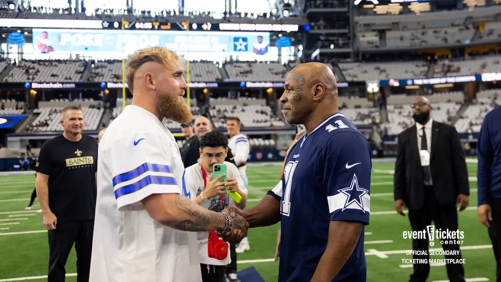Mike Tyson and Jake Paul shaking hands on the field of AT&T Stadium in Dallas Cowboys Jerseys.